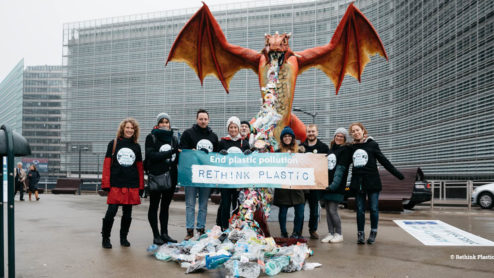 A group of 9 people campaigning in the front of a building, with a big dragon expelling fire made of plastic.